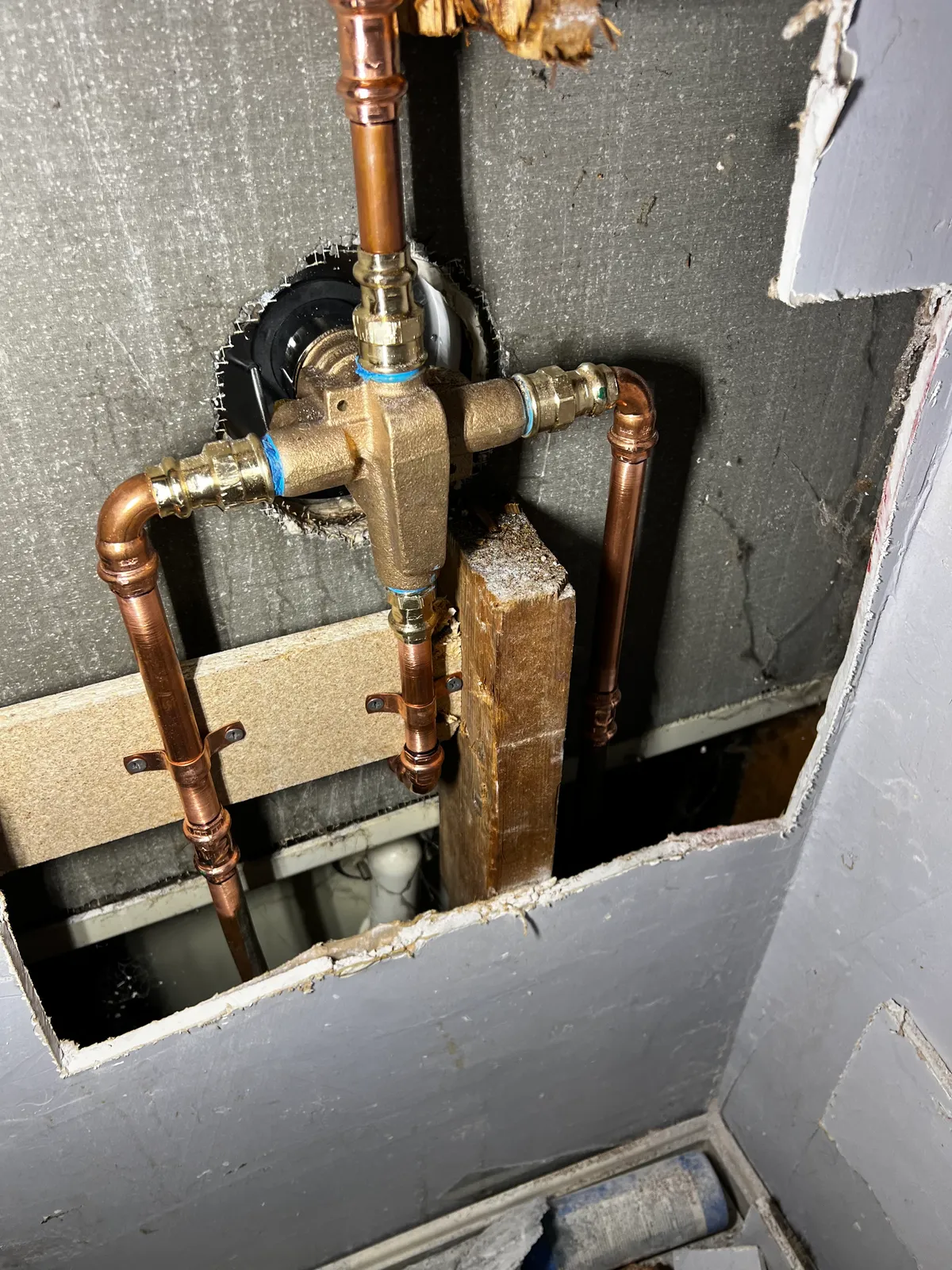 A brass shower mixing valve set into an opened wall cavity, with new copper hot and cold lines and a riser to the shower head made up with press-fit joints, clipped to the stud and backer board around it.